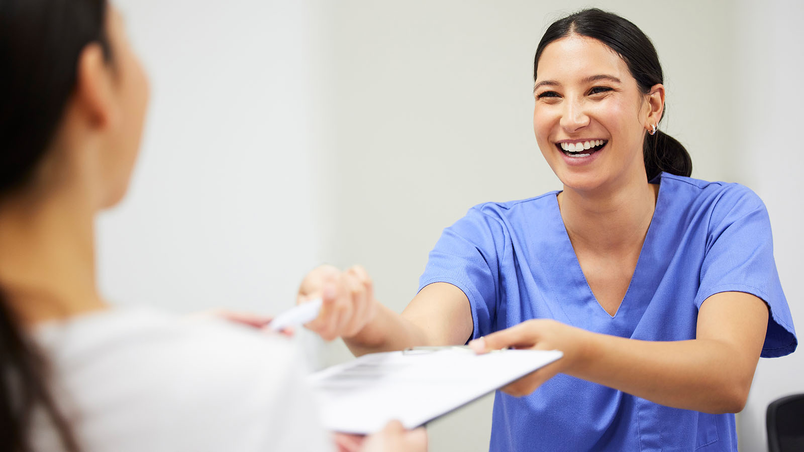 Smiling woman nurse handing a clipboard to a patient.