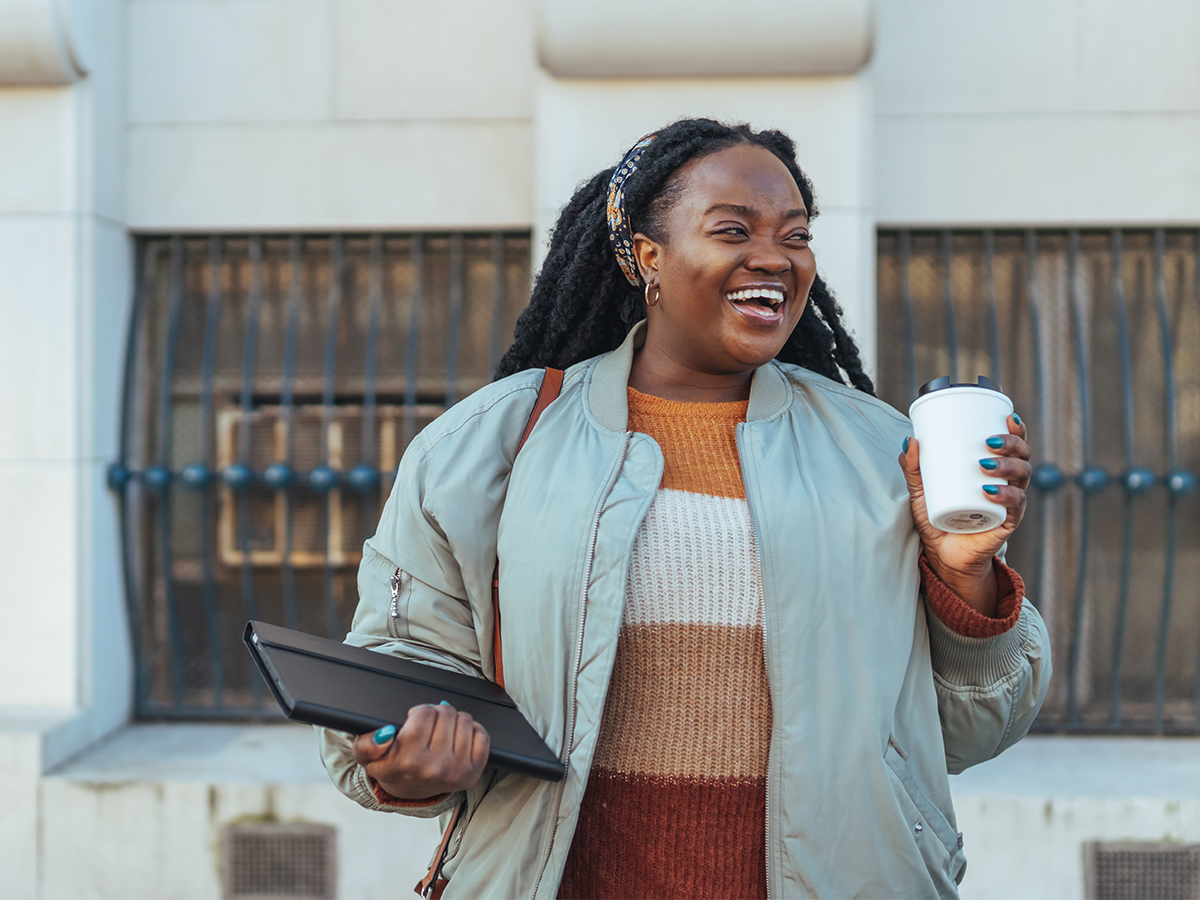 Smiling woman with tablet in one hand and coffee cup in the other