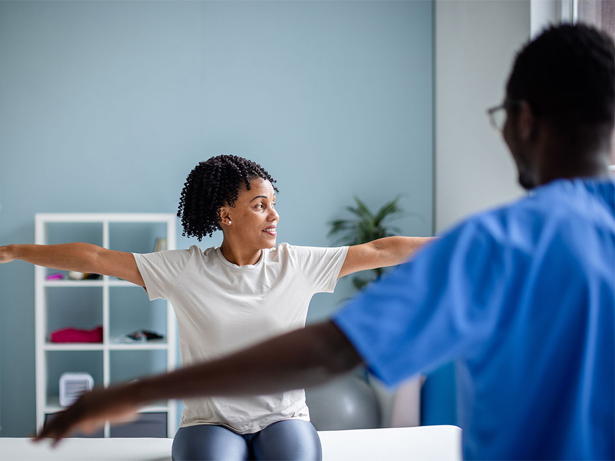 Young male physician showing female patient how to stretch her arms during an exam