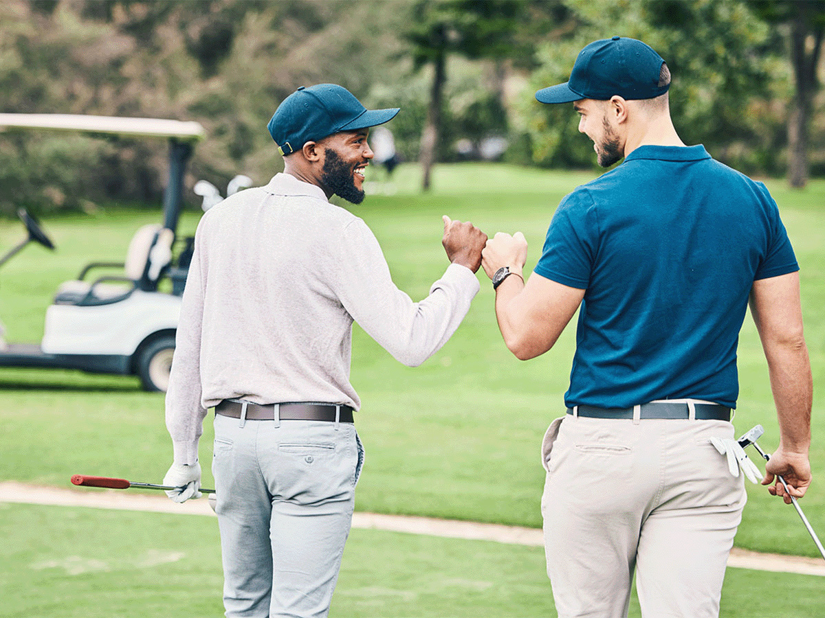 Black young male and white young male on golf course, fist-bumping and talking while walking