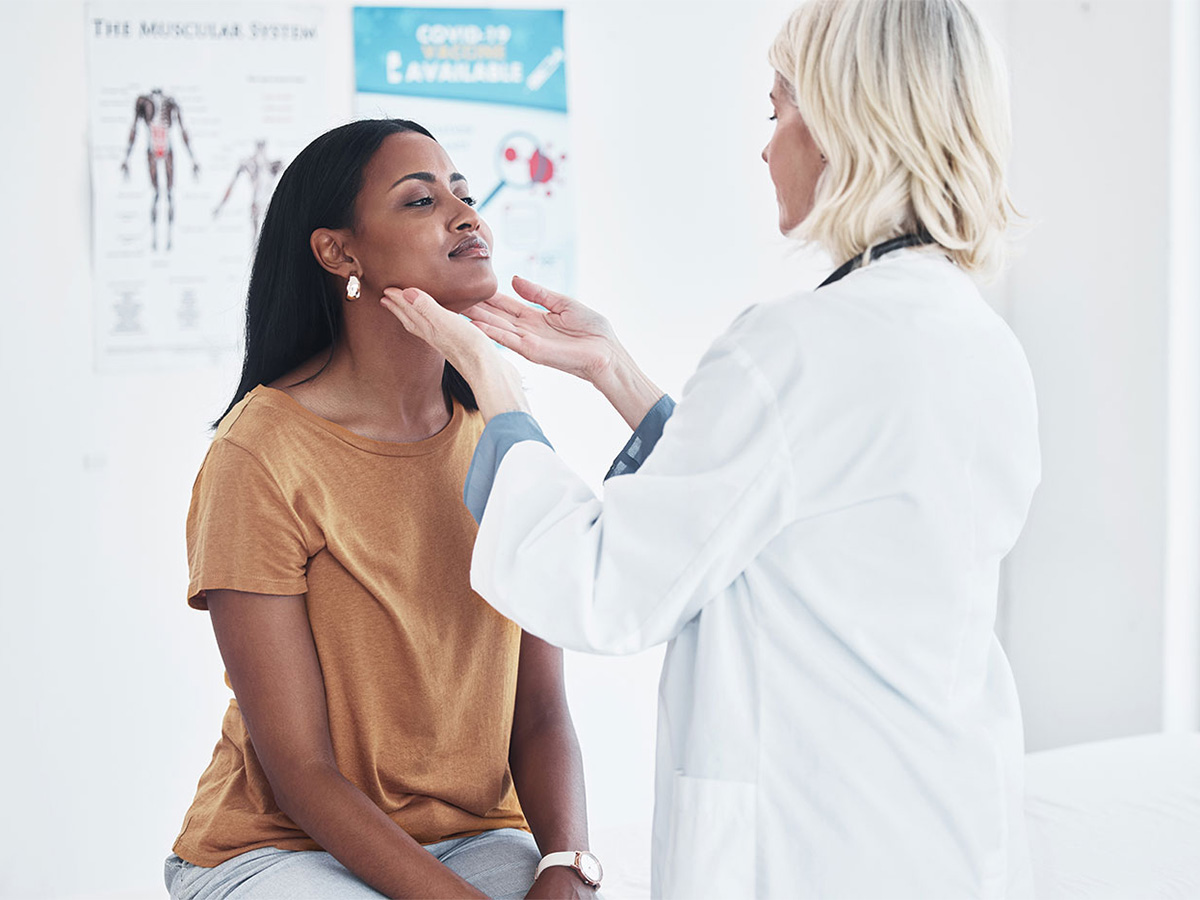 Female physician with both hands under female patient's chin to examine her neck