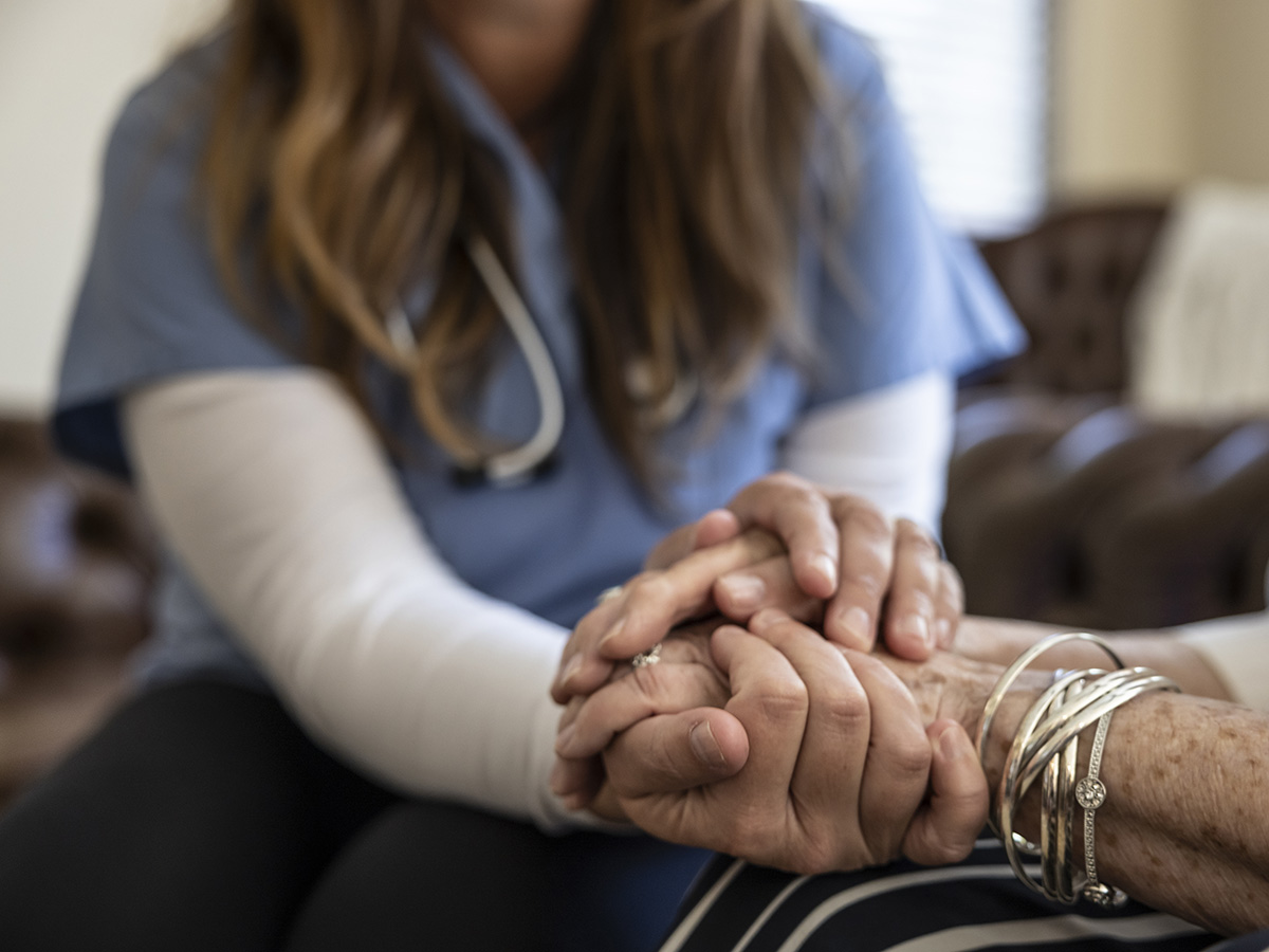 Female nurse holds the hand of an older woman