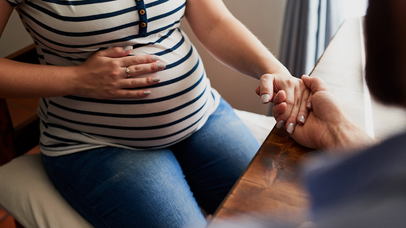 Pregnant woman with hand on stomach while holding hands with supporter