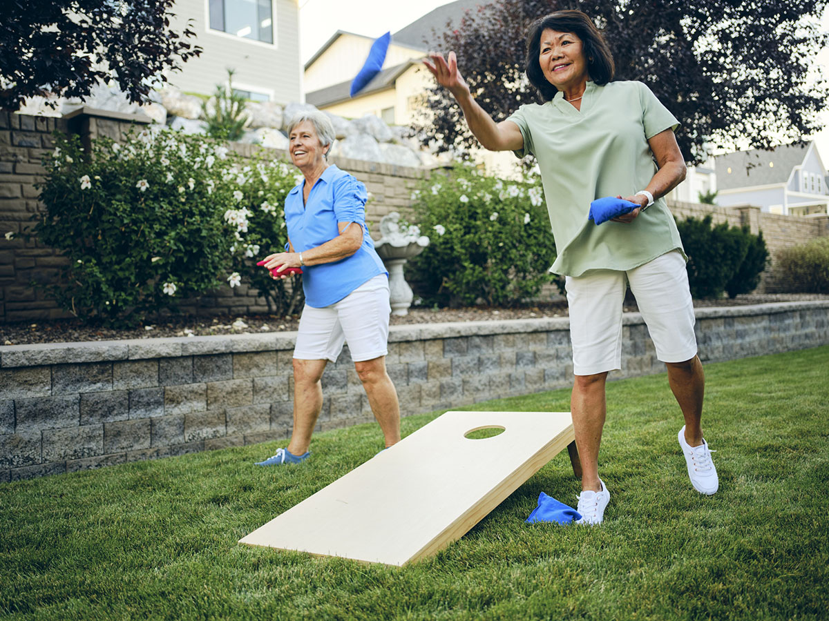 Two women outside playing cornhole game