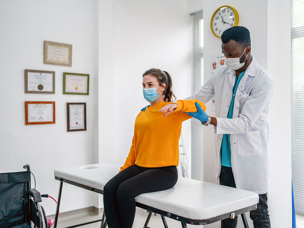 doctor treating injured arm of young woman patient in clinic