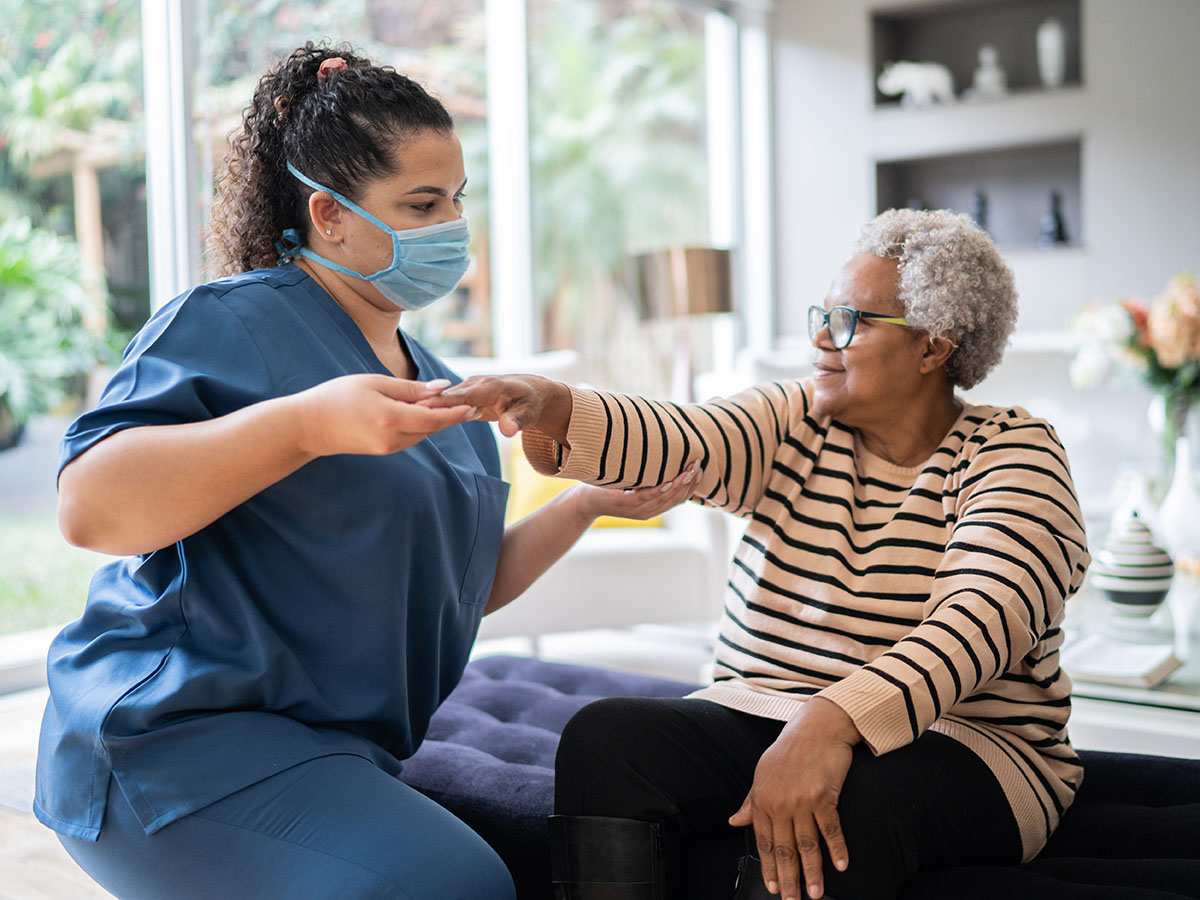 nurse wearing a face mask supports senior woman doing arm exercise