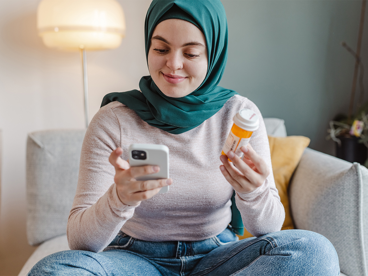 Woman in headscarf smiling while checking on medication on her phone