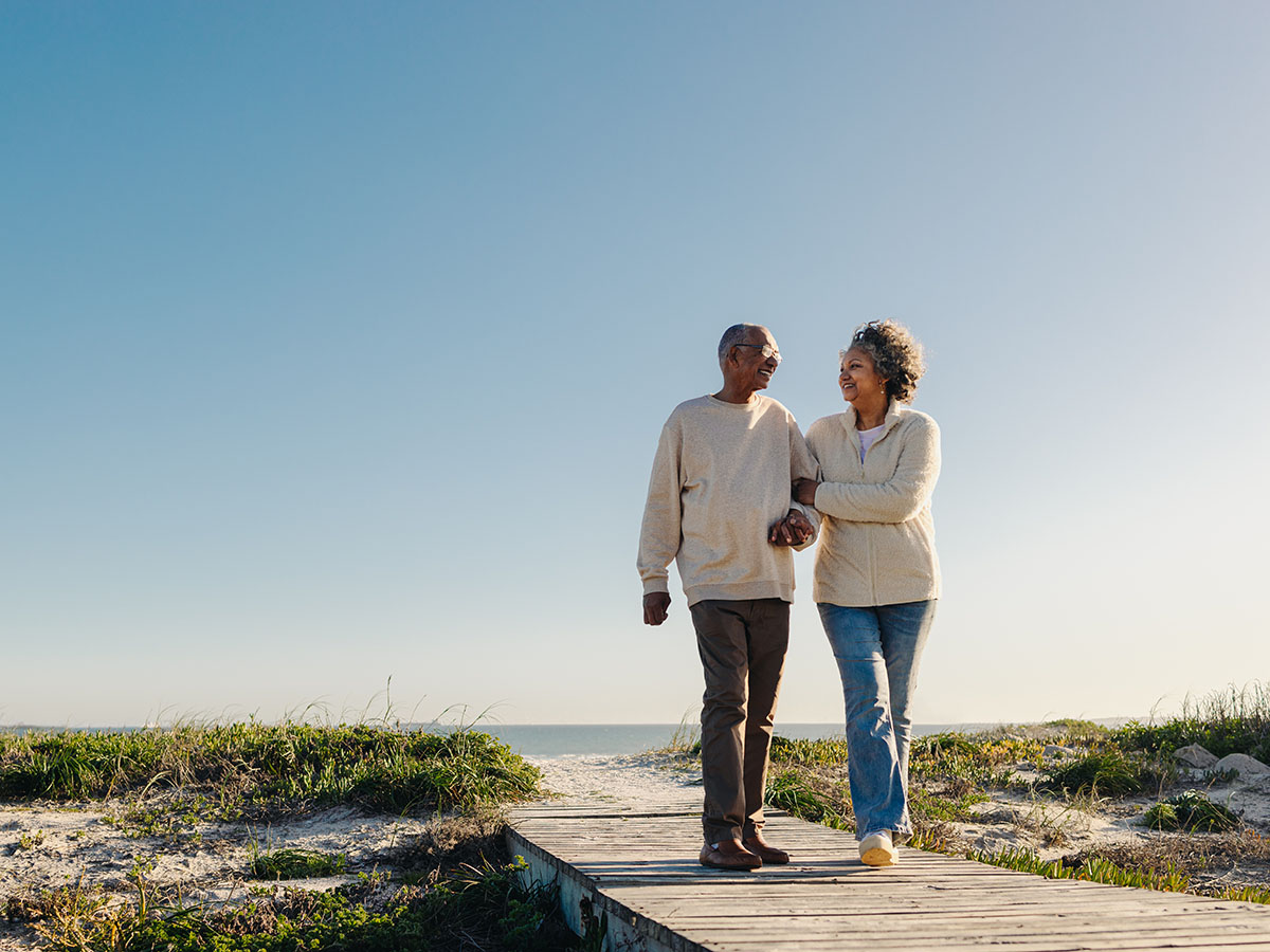 Adult couple wearing tan sweaters walking on beach