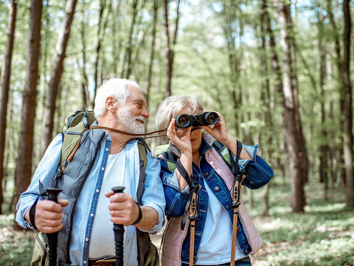 Senior couple hiking in forrest with binoculars