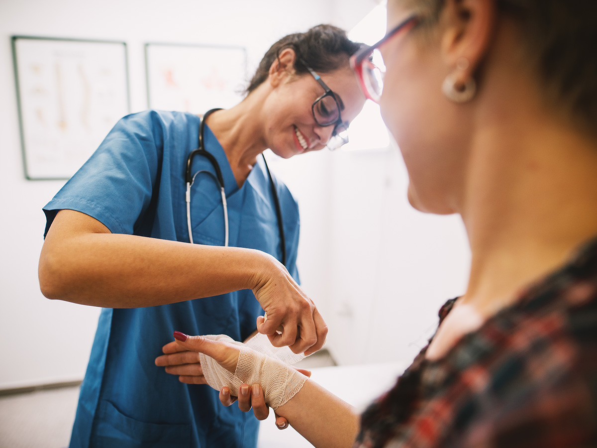 Professional nurse at the hospital bandaging the hand with a medical bandage for a woman patient.