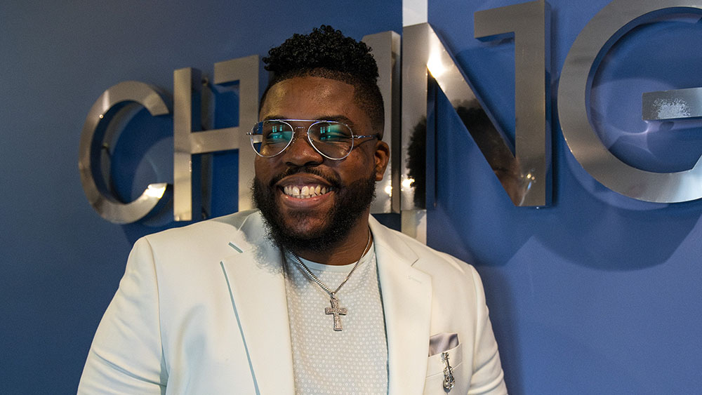 Justin, a 30-something Virtua Cardiology patient, poses in a suite in front of a logo sign at an event