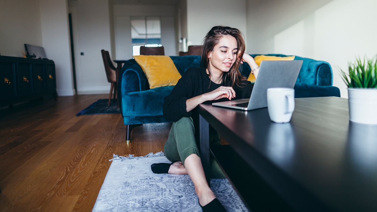 Young adult woman sits on the floor while working on her laptop