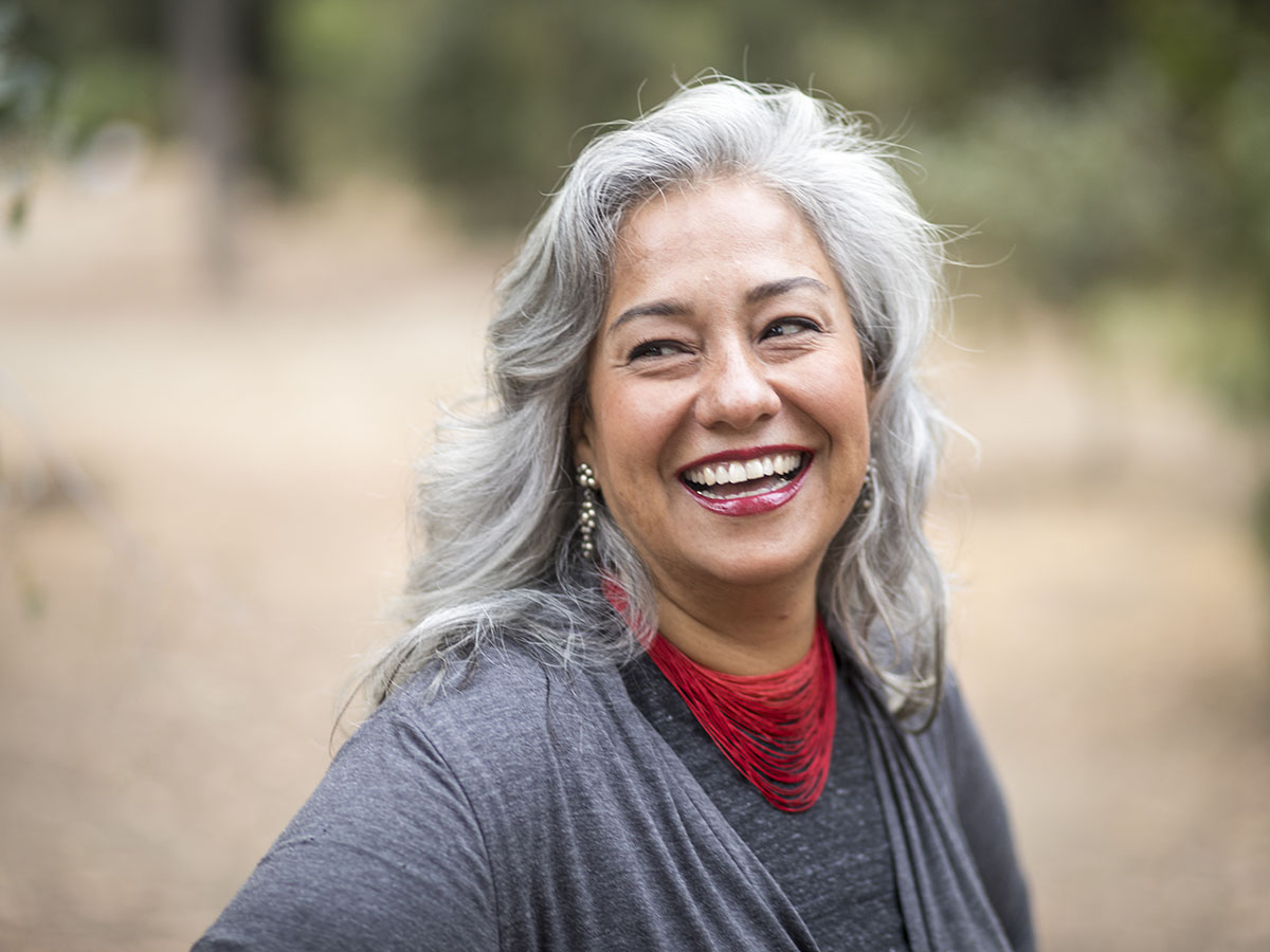 Older woman smiles outside wearing a gray shirt