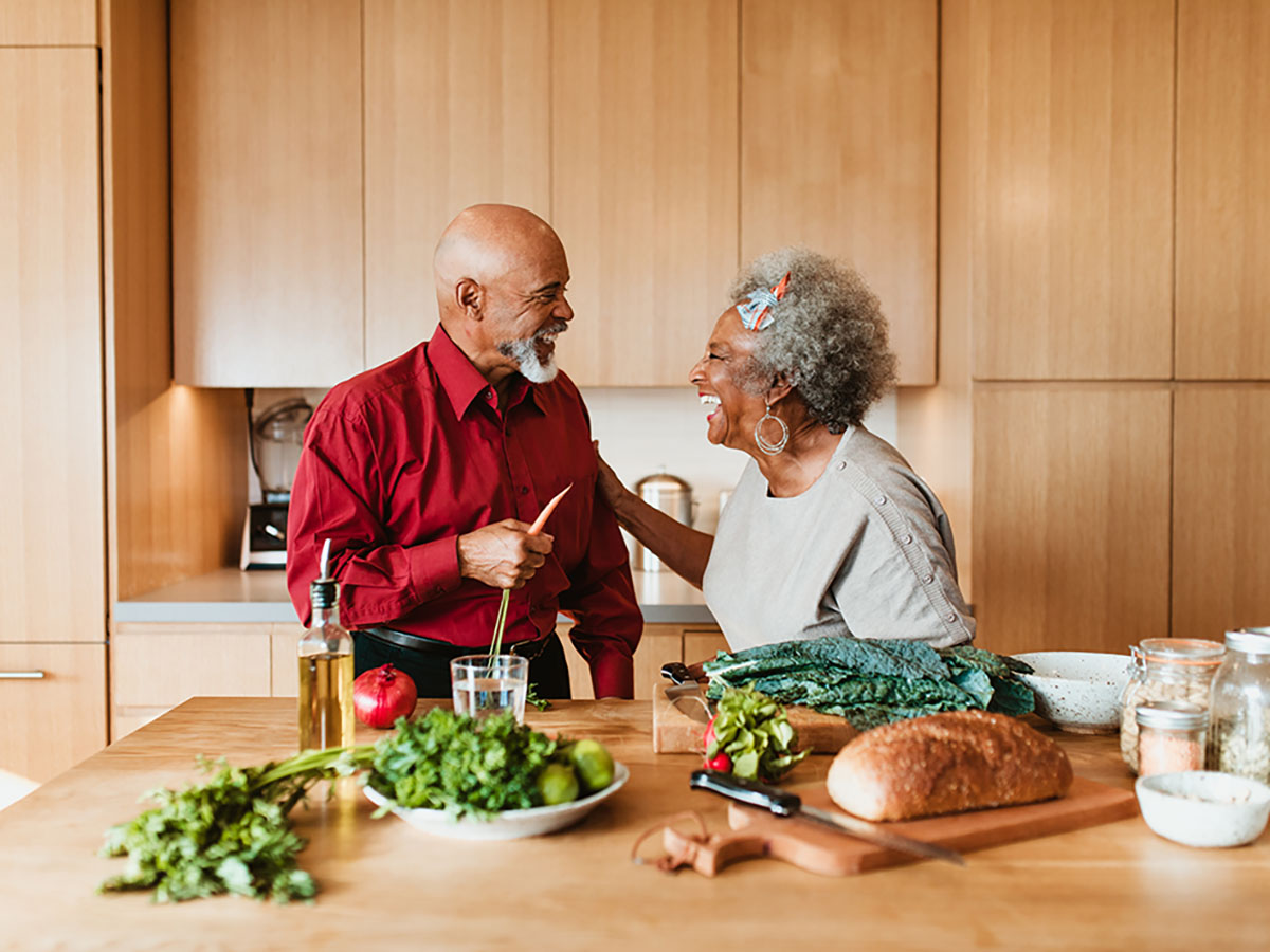 Older African-American couple laughs together while making a healthy dinner